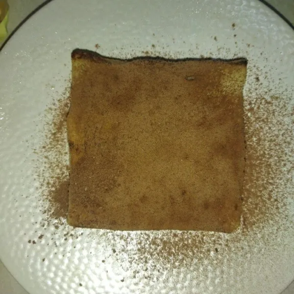 Tata roti yang sudah dipanggang di atas piring saji, taburi roti dengan cokelat bubuk secukupnya.
