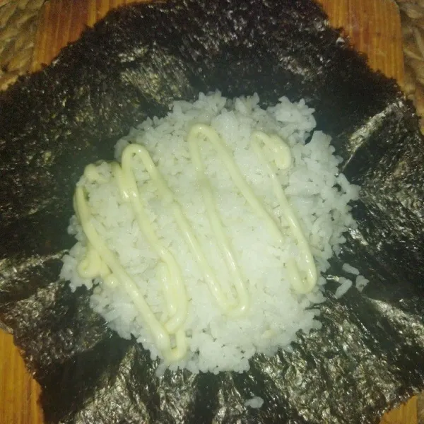 Siapkan 1 lembar nori sushi, lalu tata nasi secukupnya, bentuk nasi mirip kotak, lalu beri mayones secukupnya.