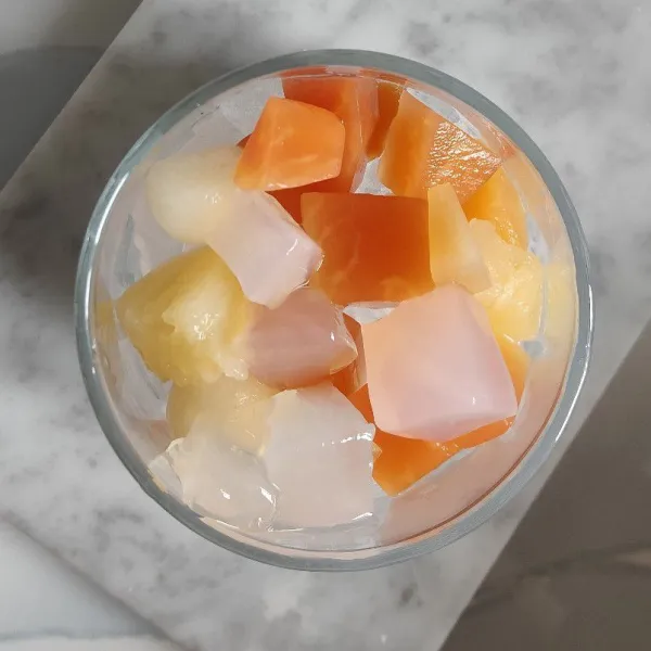 Taruh buah pepaya, buah nanas, buah apel, dan nata de coco ke dalam gelas.