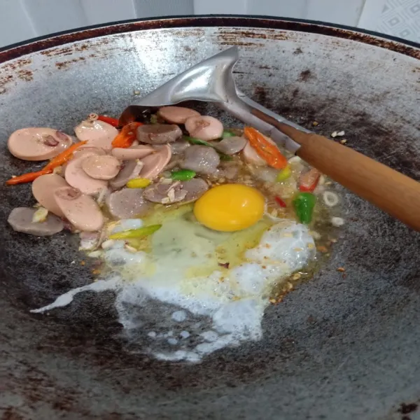 Masukkan telur lalu orak arik, kemudian masukkan irisan baso dan sosis.  Masak kembali hingga matang