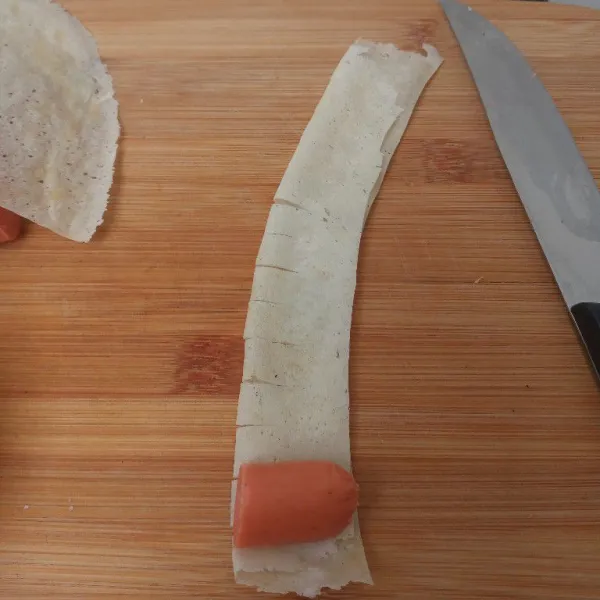 Taruh 1 potong sosis di salah satu sisinya lalu gulung dan ujungnya oles larutan tepung terigu sebagai perekat.