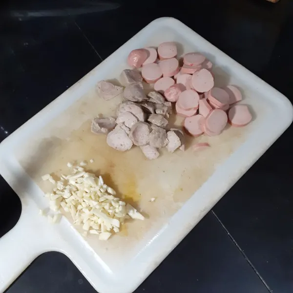 Potong-potong sosis dan bakso bentuk koin. Cincang bawang putih.