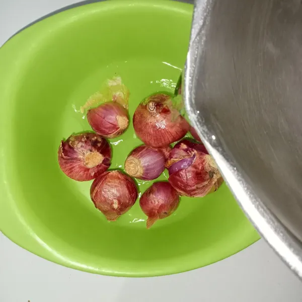 Tuang air panas ke dalam wadah berisi bawang merah.