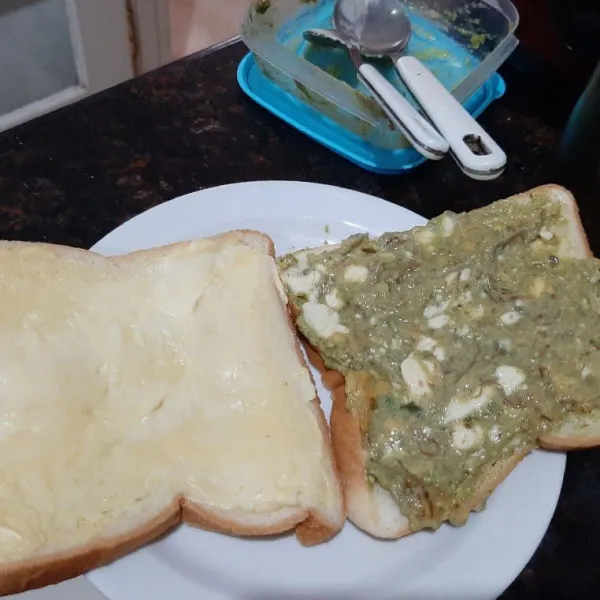 Oles satu lembar roti dengan margarine dan 1 sdm keju oles, lalu satu lembar lainnya dengan campuran alpukat keju, tumpuk kedua lembar roti dan potong menjadi 2 berbentuk segitiga