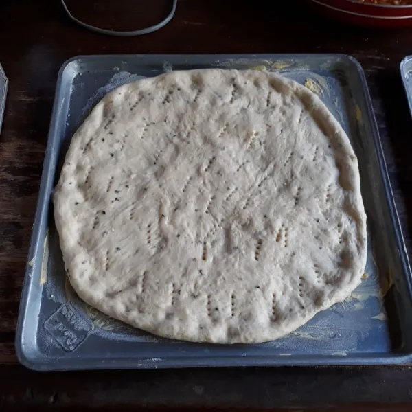 Olesi loyang dengan margarin dan taburi tipis tepung terigu. Kempiskan adonan dough dan pipihkan bentuk bulat. Tusuk-tusuk dengan garpu, diamkan 10 menit.