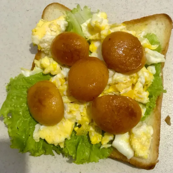Tata isian (salada, telur, dan sosis) di atas roti yang telah dipanggang.