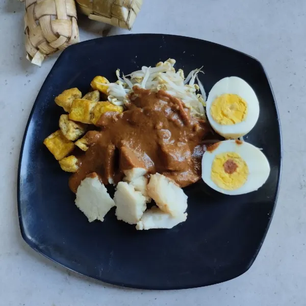 Potong-potong ketupat, tambahkan tahu bandung, taoge rebus dan telur rebus lalu siram dengan bumbu kacang. Sajikan hangat.