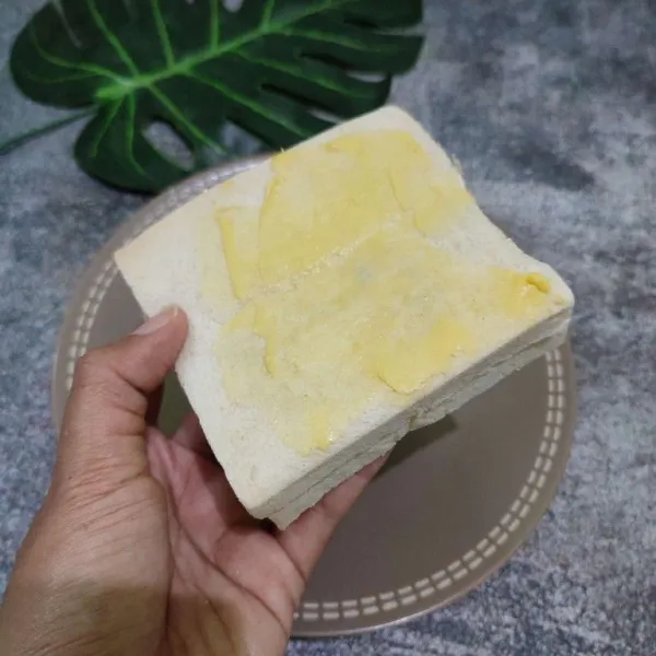 Tangkupkan roti tawar kemudian oles permukaan atasnya dengan margarin.