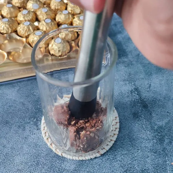 Siapkan gelas saji, masukkan coklat ferero ke dalam gelas, kemudian tekan-tekan sampai halus.