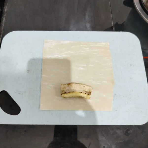 Ambil satu lembar kulit lumpia. Lalu beri satu potong pisang di ujungnya.
