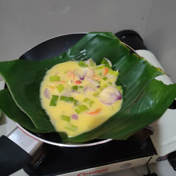 Siapkan daun pisang di pan, kemudian masak telur di atas daun pisang, tutup pan hingga telur matang.