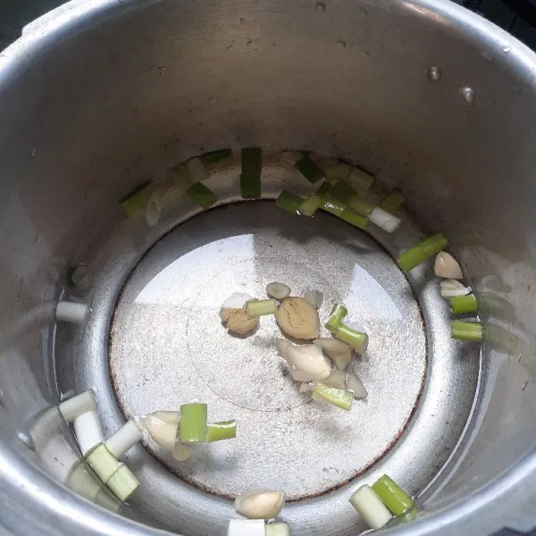Masukan air, bawang putih, jahe dan daun bawang dalam panci presto.