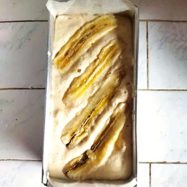 Siapkan loyang anti lengket beralas kertas roti yang sudah diolesi sedikit minyak dan masukkan adonan cake masing2 seberat 130 gr, ratakan. Beri topping pisang.