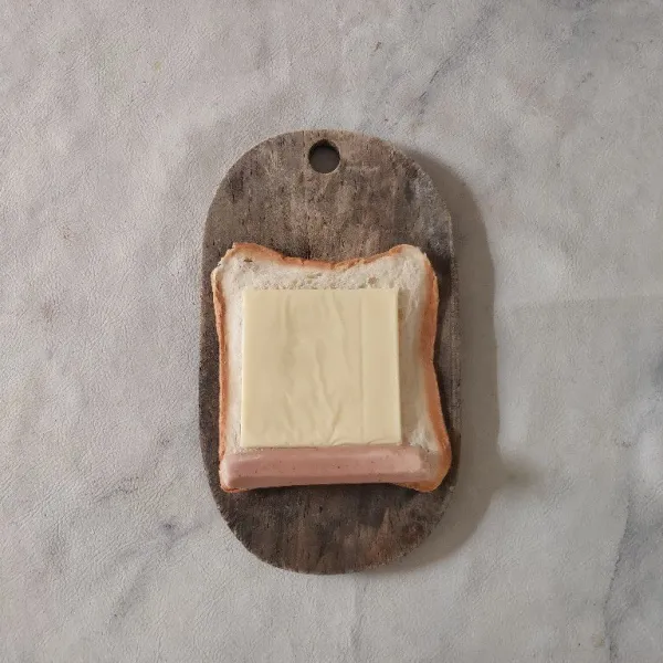 Letakkan satu lembar keju dan sosis di tepi roti.
