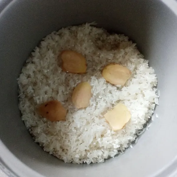 Siapkan beras yang sudah dicuci bersih. Masukkan ke dalam panci rice cooker. Tata potongan jahe.