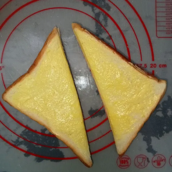 Kemudian tutup rapat roti dan olesi kedua sisi roti dengan margarin kemudian potong posisi segitiga.