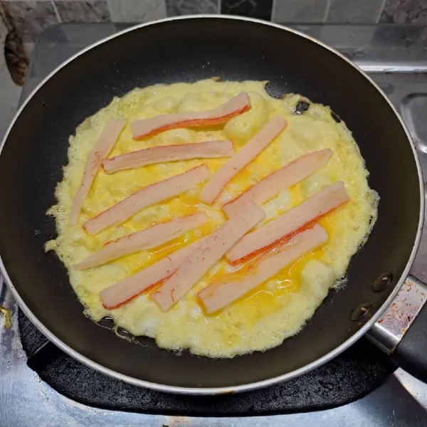Beri irisan surimi, lalu masak sampai bagian bawah berkulit. Balik adonan telur. Masak sampai matang. Angkat dan sajikan.