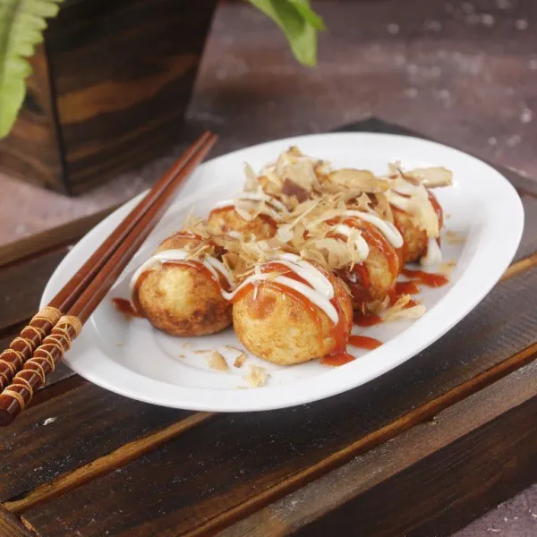 Penyelesaian, letakkan takoyaki di piring, beri topping saus dan mayonaise lalu beri taburan katsuobushi