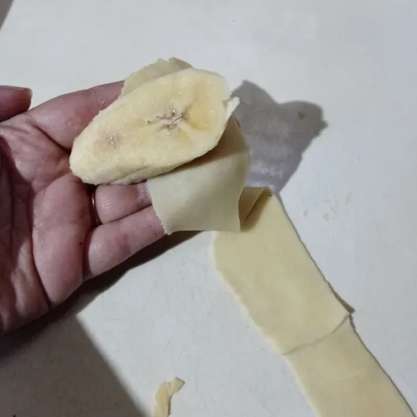 Ambi selembar potongan adonan gilas lagi sampai tipis lagi, beri isian pisang lalu gulung