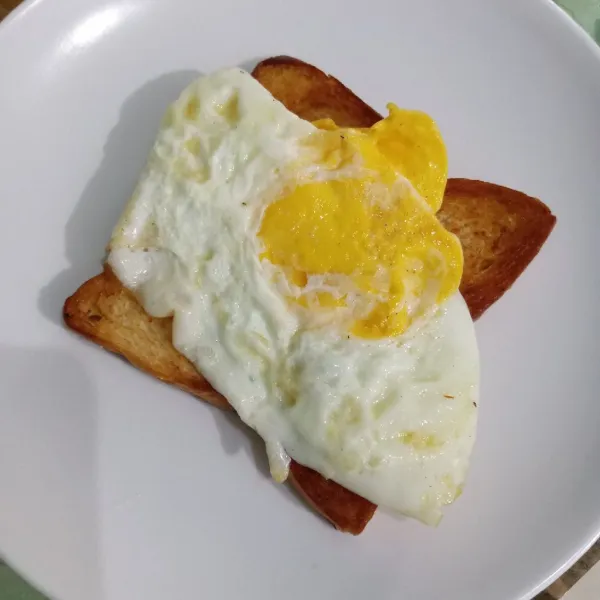 Tata roti dalam piring, beri telur ceplok di atasnya.