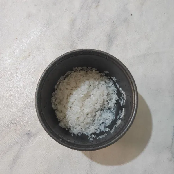 Cuci bersih beras, lalu masukkan ke dalam rice cooker.