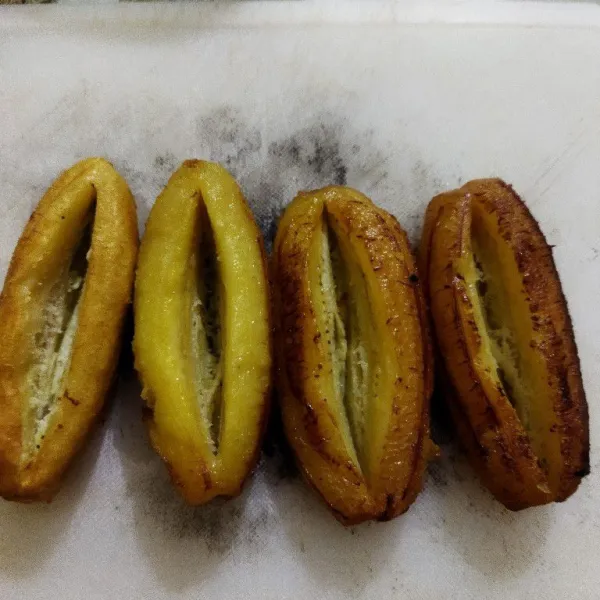 Setelah pisang agak dingin, belah tidak putus bagian tengah pisang