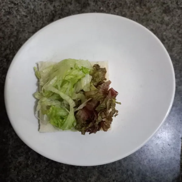 Tata irisan daun selada dan lettuce di atasnya.
