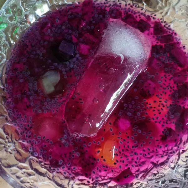 Masukkan jelly, biji selasih dan es batu ke dalam mangkuk yang berisi buah naga, kemudian tuang air gula, aduk rata.