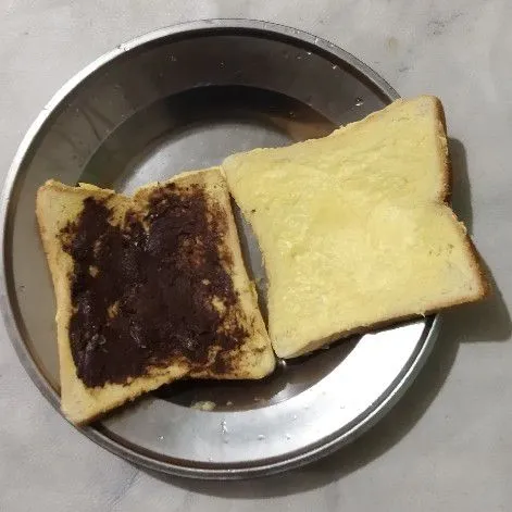 Olesi selai coklat pada salah satu roti.