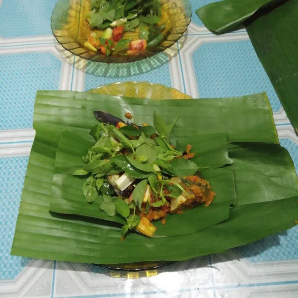 Siapkan daun pisang. Taruh ikan lalu beri kemangi, daun bawang, tomat, dan cabai rawit.