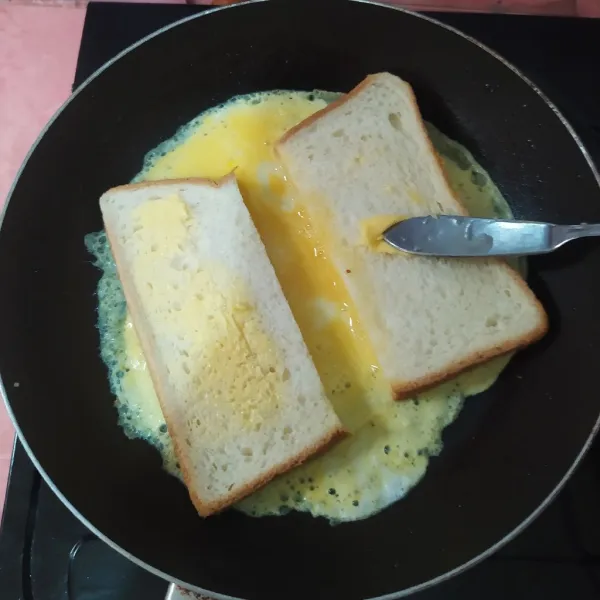 Selagi telur masih basah, tata potongan roti diatasnya dan beri jarak. Olesi roti dengan margarin.