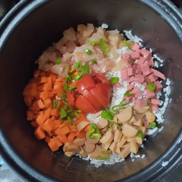 Masukkan beras ke dalam rice cooker, tambahkan tomat, sosis, kornet, ayam, daun bawang dan tomat.