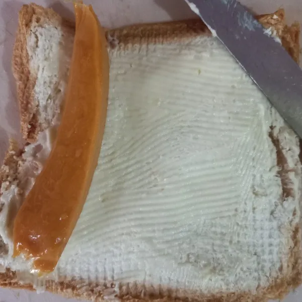 Ratakan 1 sdm keju spreedy di atas roti, tambahkan satu iris sosis, kemudian gulung.