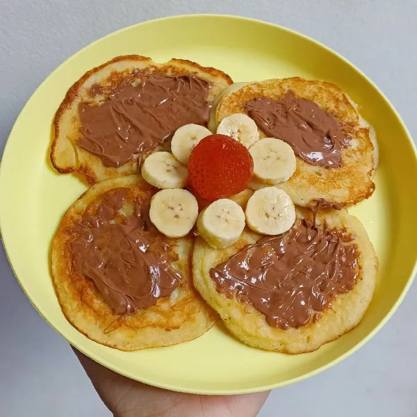 Susun pancake yang sudah matang di atas piring.

Olesi dengan selai cokelat, pisang yang sudah dipotong potong dan stroberi.

Sajikan 😄