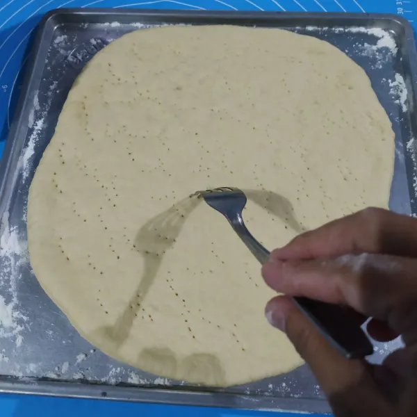 Taburi tepung terigu ke atas loyang, lalu letakkan adonan ke atas loyang. Tusuk adonan dengan garpu ke semua permukaan adonan.