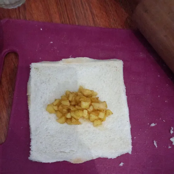 Taruh isian apel di atas roti, beri larutan tepung terigu di pinggiran roti sebagai perekat, kemudian lipat roti tawar, tekan dengan garpu di seluruh pinggiran roti tawar.