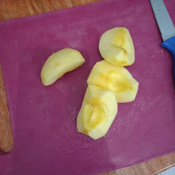 Kupas kulit apel, belah buah apel menjadi beberapa bagian.