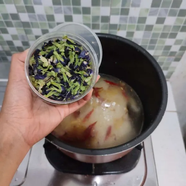 Masukkan bunga telang, aduk rata. Masak di dalam rice cooker. Jika air mulai mendidih, aduk rata nasi agar air telang tercampur merata.