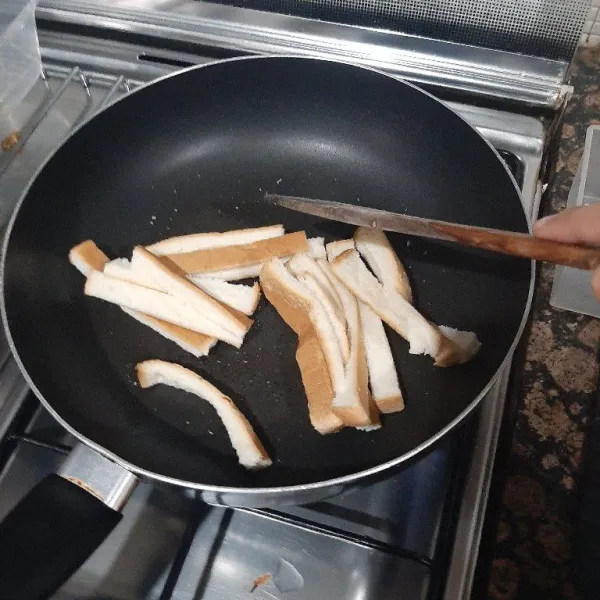 Potong pinggiran roti memanjang/setiap 1 lembar roti tawar kotak jadi 4 pinggiran roti. Panggang pinggiran roti di atas pan tanpa menggunakan minyak/mentega. Aduk sesekali, hingga pinggiran roti berubah kecoklatan dan garing.