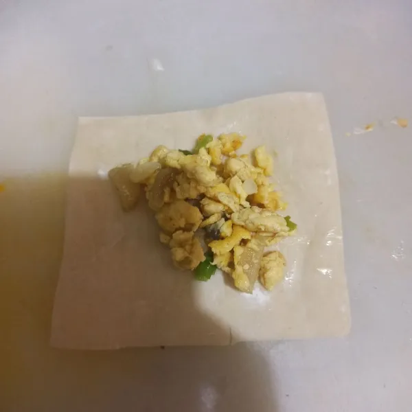 Ambil kulit pangsit, lalu beri scramble egg di tengah. Lalu beri air atau bisa juga larutan tepung di pinggiran kulit pangsit.