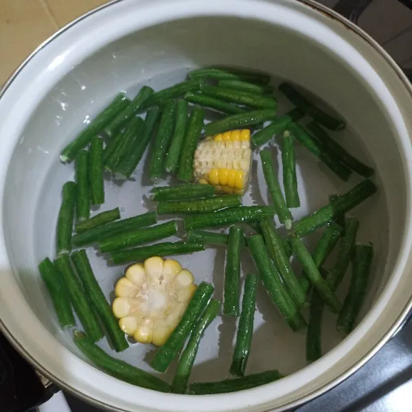 Didihkan air dalam panci, lalu masukkan potongan jagung dan kacang panjangnya.