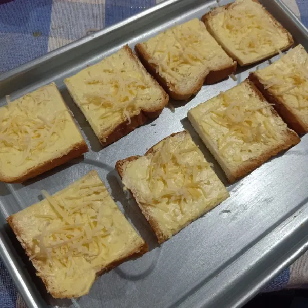 Taburi keju parut dan tata roti di loyang lalu panggang sampai matang.