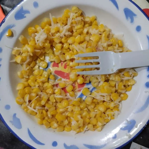 Pindahkan jagung manis ke piring, beri sebagian keju parut dan kental manis. Aduk rata.