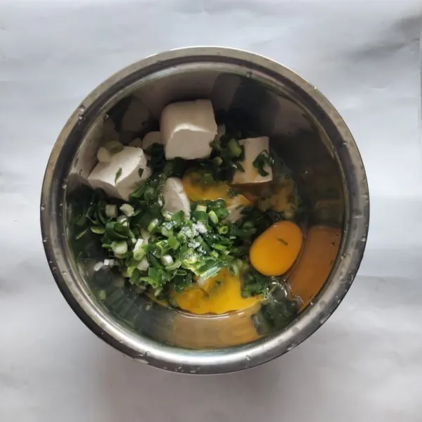 Siapkan wadah, kemudian masukkan tahu putih, telur ayam, irisan daun bawang, garam, dan kaldu jamur.