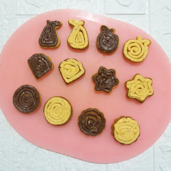 Beri pasta coklat di bagian bawah cookies dan pasta keju di bagian bawah cookies lain yang bentuknya sama.