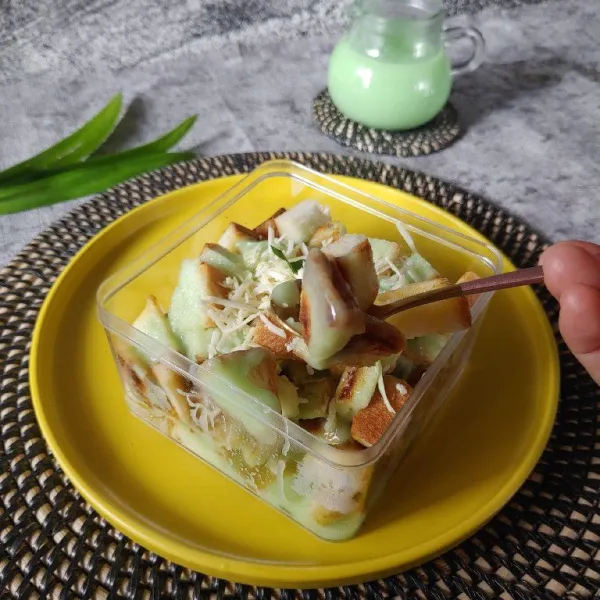 Masukkan roti kedalam wadah, siram dengan kuah pandan. Beri toping keju parut. Sajikan.