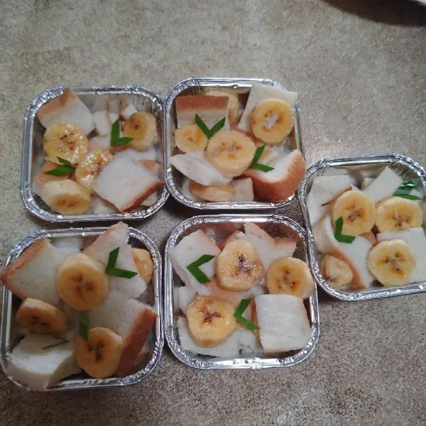 Tata roti di dalam wadah cup, tuang kuah santan dan beri potongan buah pisang dan irisan daun pandan.