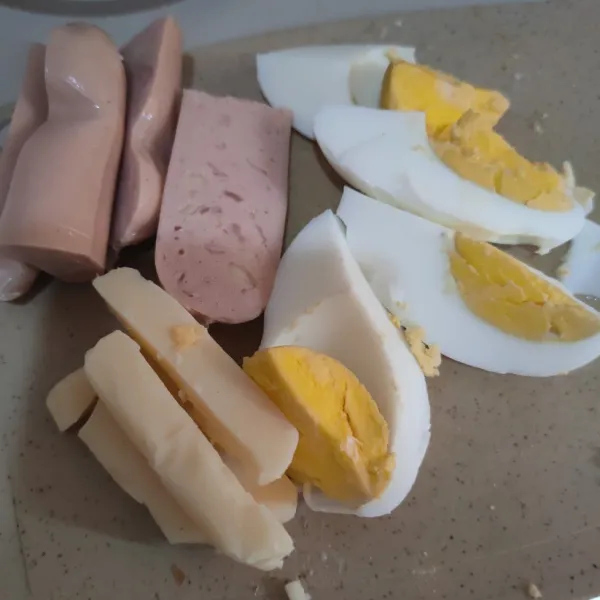 Potong memanjang sosis, telur rebus dan keju.