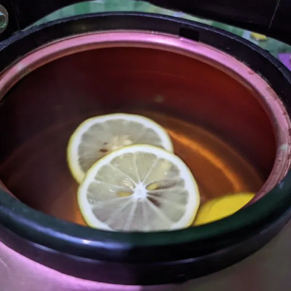 Cuci bersih lemon kemudian iris tipis, masukkan setengah irisan lemon ke dalam teko.