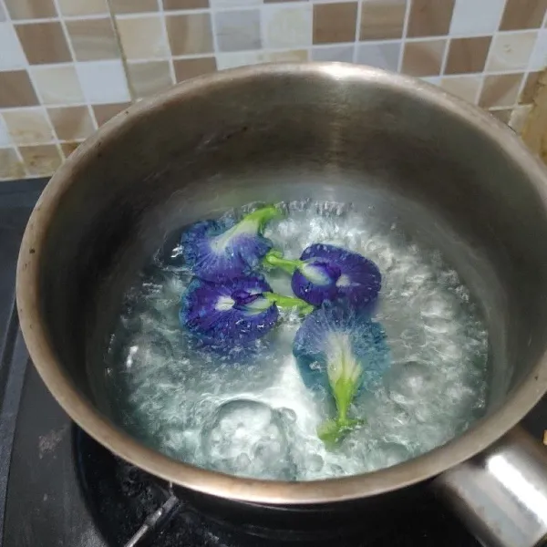 Didihkan air, masukkan bunga telang, aduk sampai keluar warnanya dan matikan api. Biarkan sampai airnya berubah warna menjadi biru dan buang sisa bunganya.